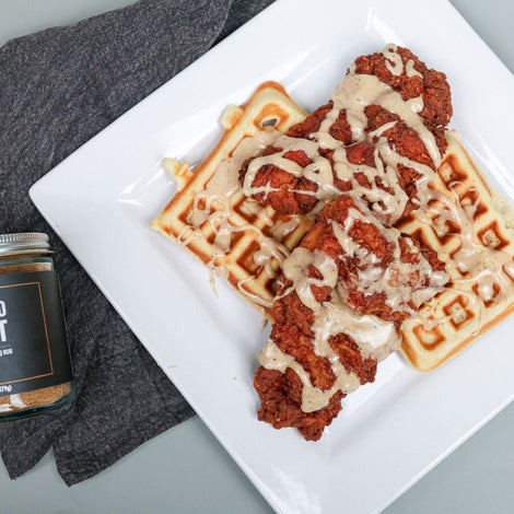 A white, square plate that has 2 square waffles and crispy chicken thighs drizzled in a maple glaze.