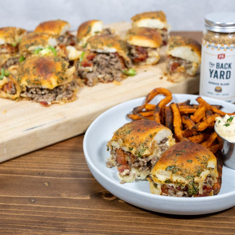 Baked cowboy sliders made with ground beef, bacon, fried onions, and melted cheese on Hawaiian rolls, seasoned with PS Seasoning Backyard Blend, served with sweet potato fries and aioli.