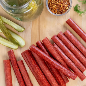 Spicy Dill Pickle Snack Sticks in front of a jar of spices and sliced pickles.