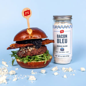 A 6.1 oz jar of Bacon Bleu Burger Blend next to a finished Bacon Bleu Signature Burger and bleu cheese crumbles. 