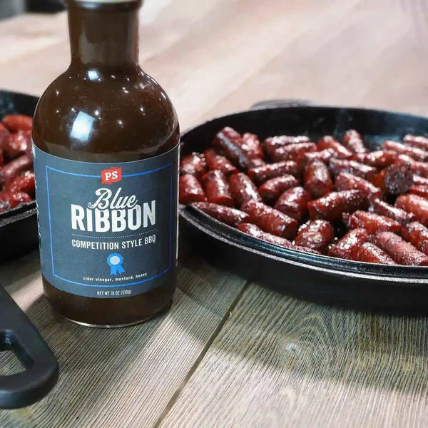 Pan of burnt ends next to a bottle of Blue Ribbon - Competition-Style BBQ Sauce