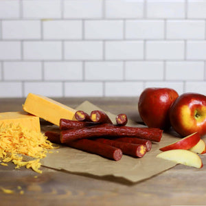 Cheddar Apple Snack Sticks laying on a paper towel next to a pair of apples and blocks of cheese.