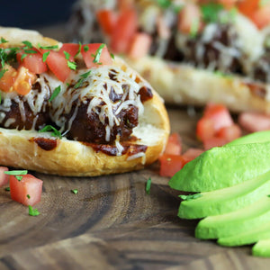 A meatball sub with mozzarella cheese, pico, and avocado on the side