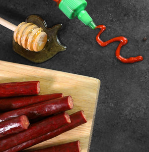 A bed of Honey Sriracha Snack Sticks next to a dripping honey comb and a bottle of sriracha.