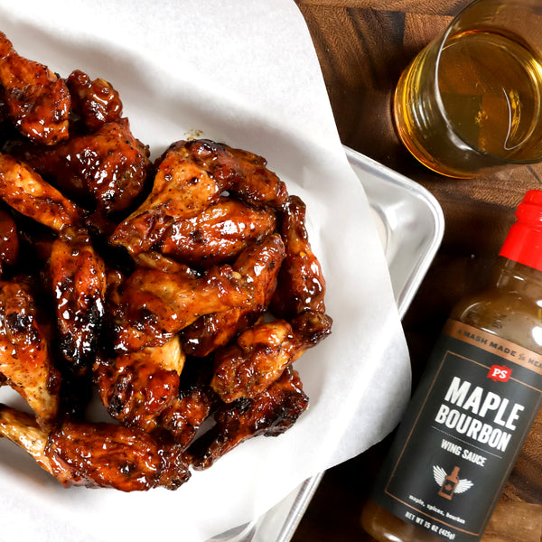 PS Seasoning's bourbon BBQ sauce used as a chicken wing sauce next to a basket of coated wings and a beer.