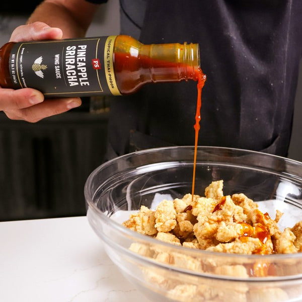 Pineapple Sriracha Wing Sauce being poured into a bowl of naked wings until fully coated.