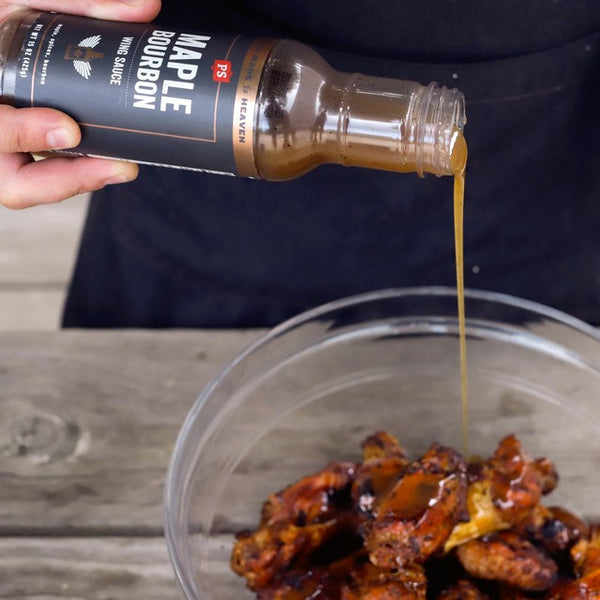 Maple Bourbon Wing Sauce being poured into a bowl of chicken wings until fully coated. 