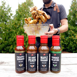 Pineapple Sriracha, Hot Honey Peach, Maple Bourbon, and Candied Jalapeno wing sauces in front of a bowl of wings being flipped.