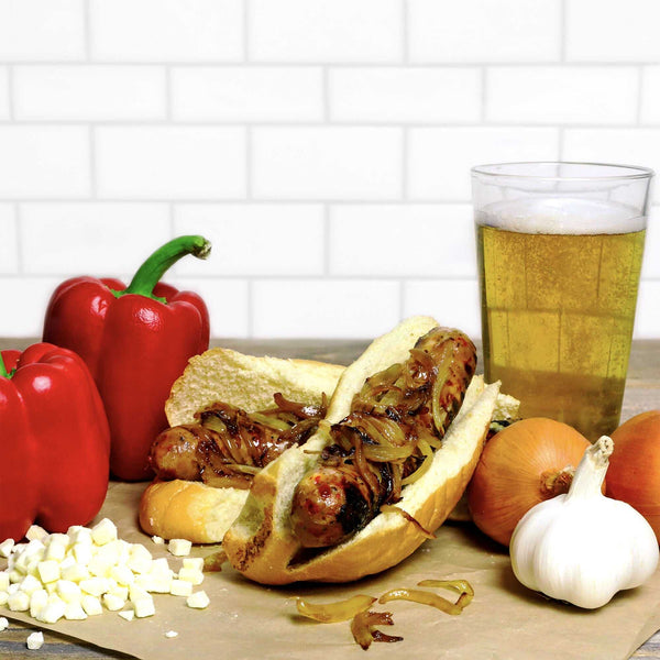 Badger Brat with onions on top of it surrounded by ingredients and a beer. 