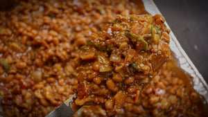 Smoked baked beans in a foil pan loaded with bacon and ground beef