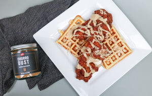 A white, square plate that has 2 square waffles and crispy chicken thighs drizzled in a maple glaze. 