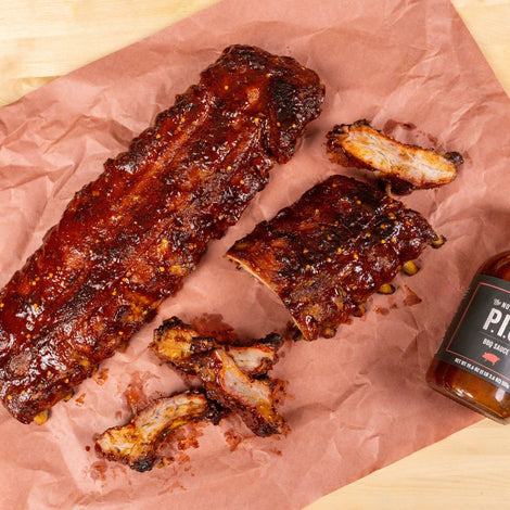 2 racks of ribs sitting on a piece of butcher paper with a bottle of PS Seasoning's Notorious P.I.G. rub along side it. 
