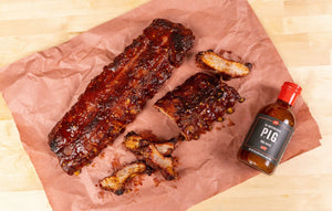 2 racks of ribs sitting on a piece of butcher paper with a bottle of PS Seasoning