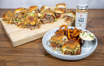Baked cowboy sliders made with ground beef, bacon, fried onions, and melted cheese on Hawaiian rolls, seasoned with PS Seasoning Backyard Blend, served with sweet potato fries and aioli.
