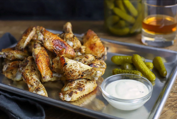Grilled or baked chicken wings seasoned with PS Seasonings The Backyard buttery burger rub. Served on a metal tray with a side of ranch dressing and a small jar of pickles. Perfect for tailgating, parties, or a main meal dish.
