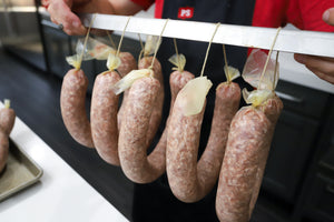 uncooked ring bologna hung on a rack for smoking