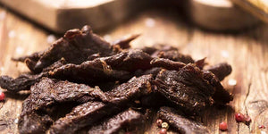 Homemade beef and venison jerky strips on a wooden board with PS Seasoning jerky kit seasoning — complete guide to making jerky in a smoker, oven or dehydrator