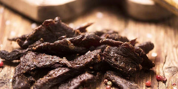 Homemade beef and venison jerky strips on a wooden board with PS Seasoning jerky kit seasoning — complete guide to making jerky in a smoker, oven or dehydrator