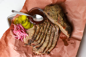 Meat that was smoked next to a bowl of BBQ sauce, pickles, and onions.