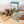 A sausage kit ingredients laid out on a light wood countertop, including a box of sausage links, a bag of seasoning mix, a package of breading sauce, garlic bulbs, and red pepper flakes, with a white subway tile backsplash behind.