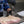 A person wearing black gloves sprinkles coarse white seasoning over a raw cut of pork belly resting on a metal baking sheet.
