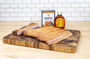 wood board with raw sliced bacon, bacon kit and bottle of maple syrup