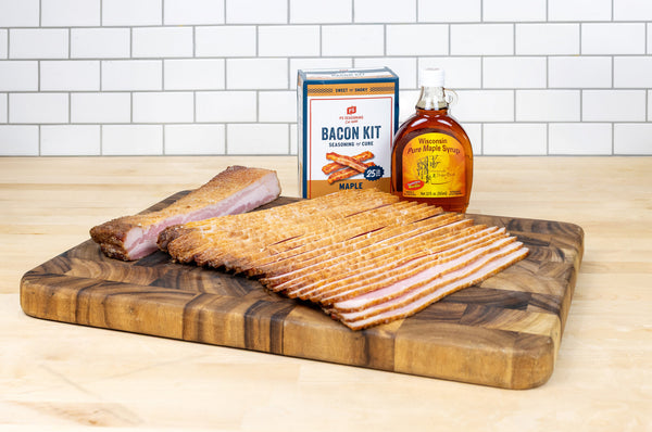 wood board with raw sliced bacon, bacon kit and bottle of maple syrup