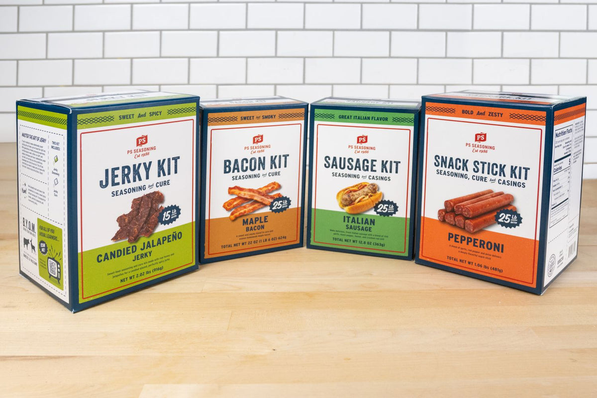 Four boxes of FS Products seasoning kits lined up on a light wood surface against a white subway tile wall: Jerky Kit, Bacon Kit, Sausage Kit, and Snack Stick Kit.