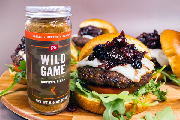 Jar of 'Wild Game' seasoning on a wooden board with burgers in the background