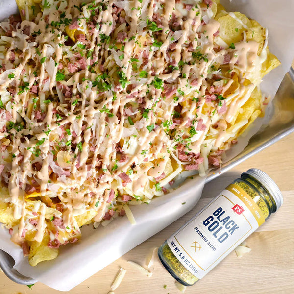 Platter of pasta with cheese and ham next to a container labeled 'Black Gold' on a wooden surface.