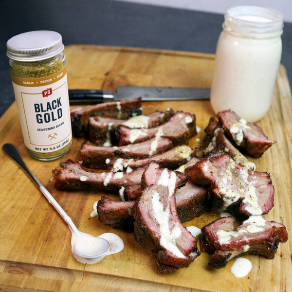 Ribs with black gold seasoning on a cutting board with a jar of black gold seasoning and a jar of milk.
