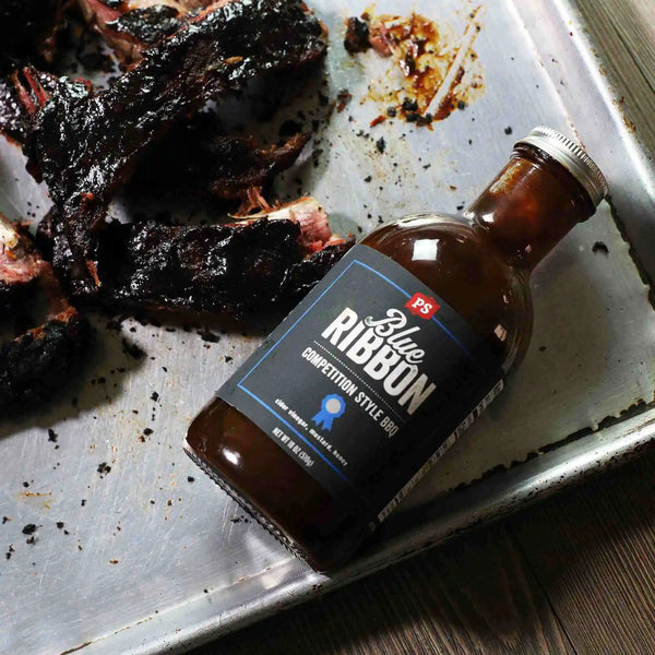 Ribs next to a bottle of Blue Ribbon - Competition-Style BBQ Sauce 