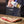 A person in a dark apron sprinkles Burled Preside seasoned salt over a raw cut of beef on a wooden cutting board.