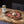 A jar of Burles Treasure Seasoning Blend sits on a wooden cutting board next to sliced cooked meat topped with a dollop of white sauce, with coarse seasoning scattered around.