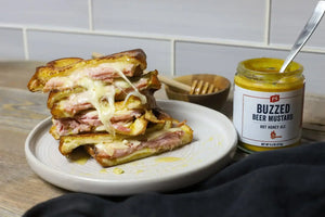 Monte Cristo Sandwhich next to an opened Buzzed Beer Mustard with a spoon in it