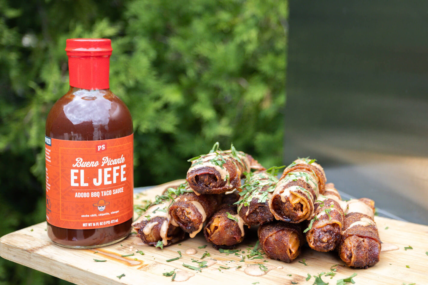 Bottle of 'El Jefe' sauce with chorizo shotgun shells on a wooden board outdoors