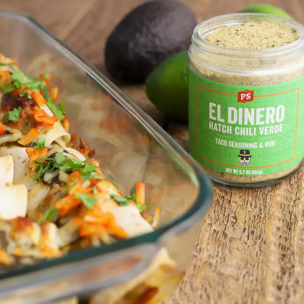 Jar of 'El Dinero' Hatch Chili Verde seasoning with a dish of taco ingredients on a wooden surface.