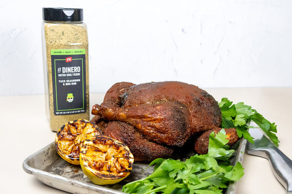 Smoked chicken on a tray with grilled lemons and a container of seasoning on a white background