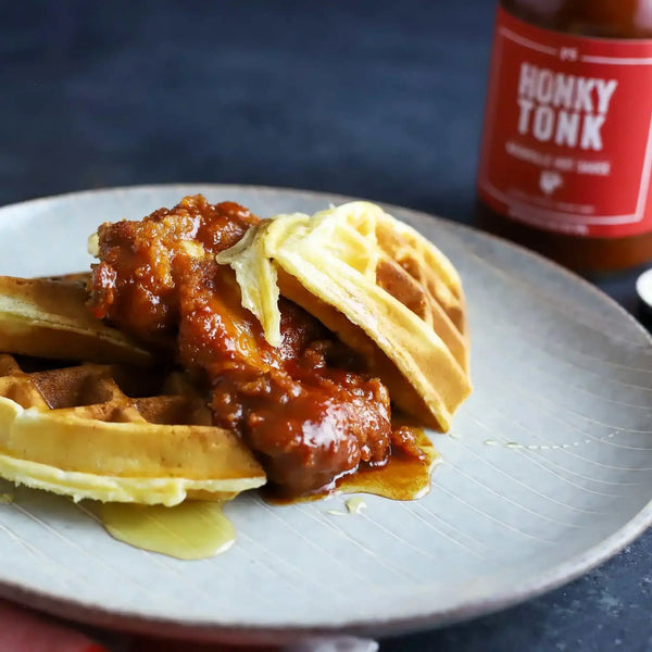 A plate of Nashville Hot Chicken and Waffles with a bottle of Honky Tonk behind it.
