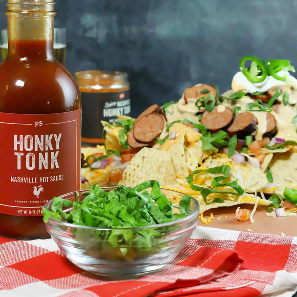 A plate of nachos with Honky Tonk - Nashville Hot Sauce and seasoning to the side of it