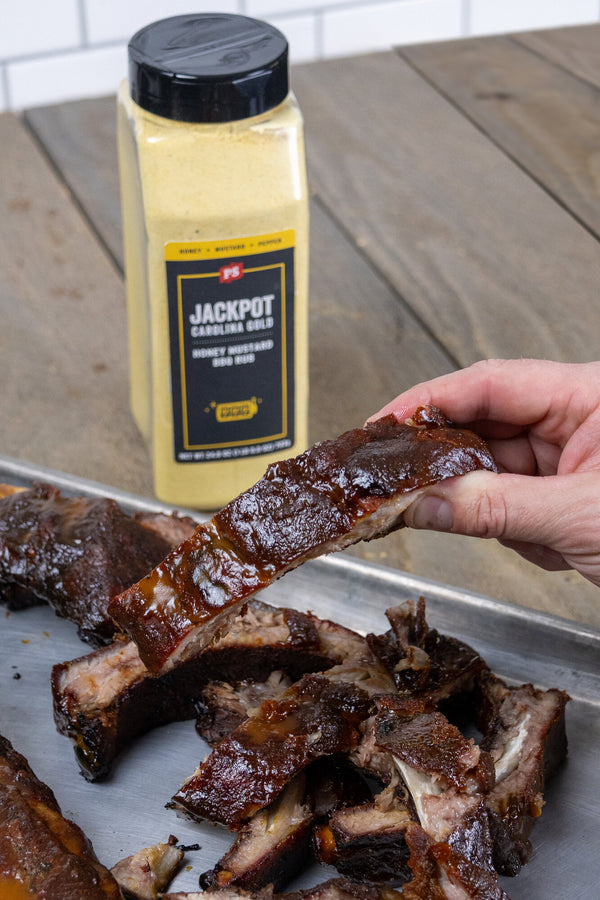 Person holding a rib next to a bottle of Jackpot Cooking Oil on a wooden table.