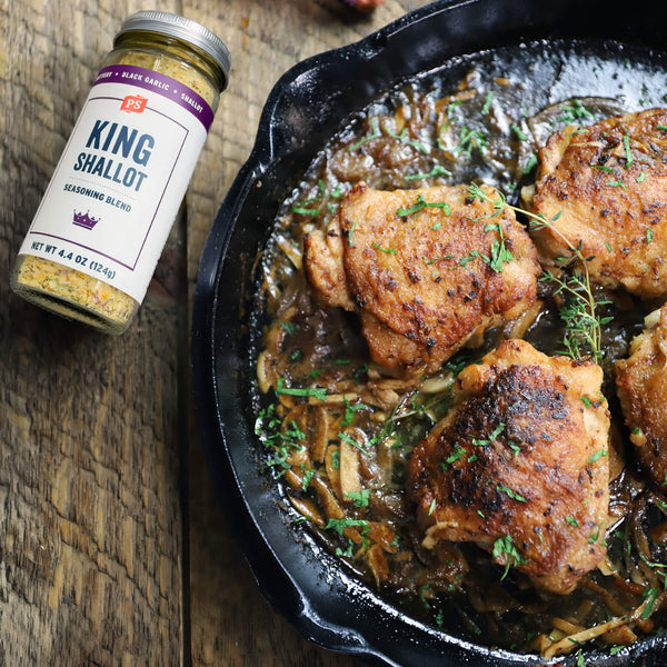 Skillet of chicken with a jar of King Shallot seasoning on a wooden surface