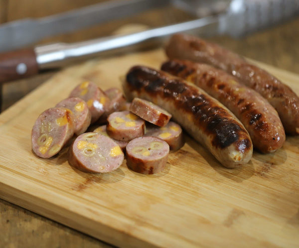 A Mac & Cheese brat cut up into small pieces next to 3 whole ones.