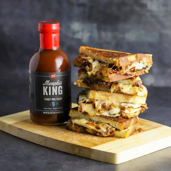 A stack of smoked brisket grilled cheese next to a bottle of Memphis King BBQ sauce