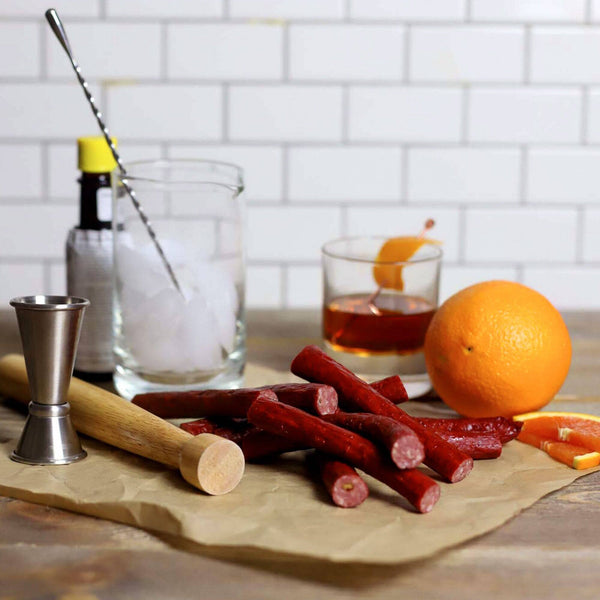  Whiskey Old Fashioned Snack Sticks next to an orange and an old fashion.