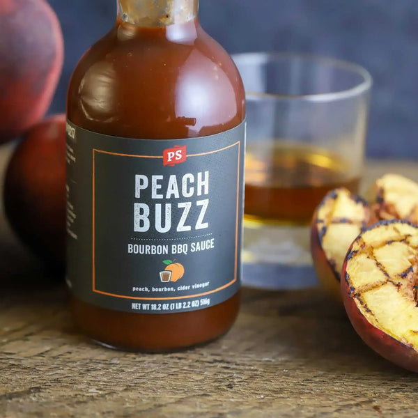 Peach Buzz in front of a glass of bourbon and next to something recently grilled.