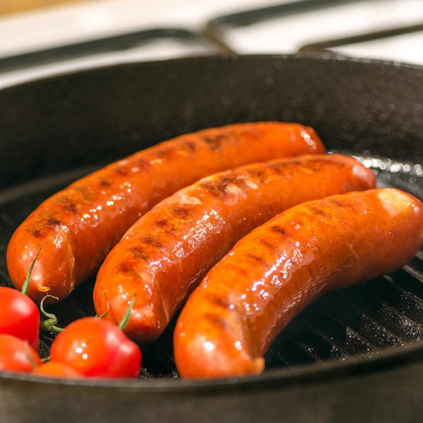 Fajita Brats cooking in a pan with a handful of tomatoes. 
