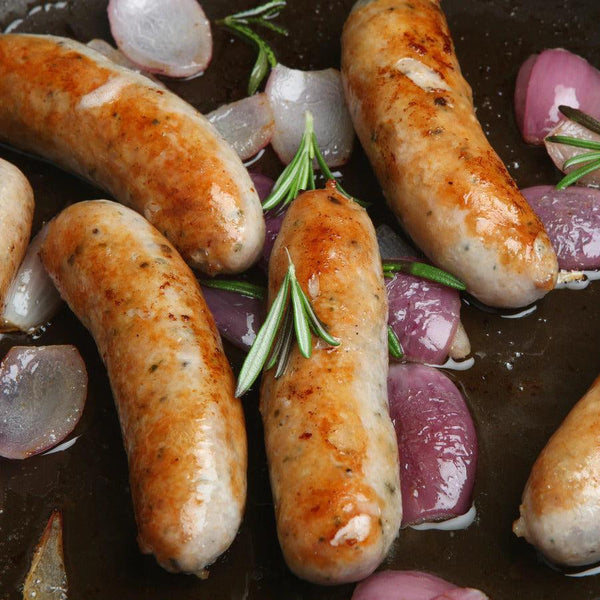 Fresh Pork Sausages being cooked in a pan rested on onions soaking in juice.