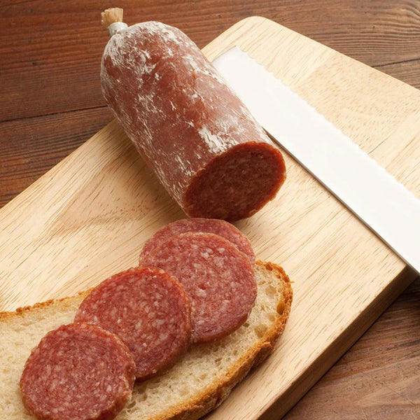 Slices of Mettwurst on a bread, with the log and knife next to it on a cutting board.