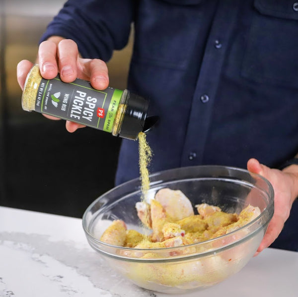 PS Seasoning Spicy Dill Pickle Dry Rub - spicy dry rub for chicken wings used on a bowl of chicken drumsticks